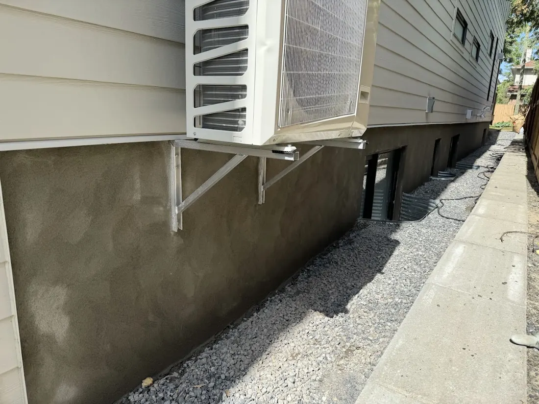 Freshly parged grey foundation wall beside a house with an air conditioner above