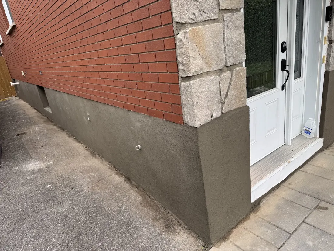 Parged dark-grey foundation below red brick beside a front door and stone steps