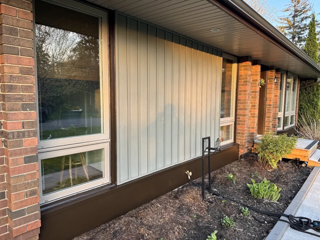 Dark parged foundation under a window and vertical siding with garden bed